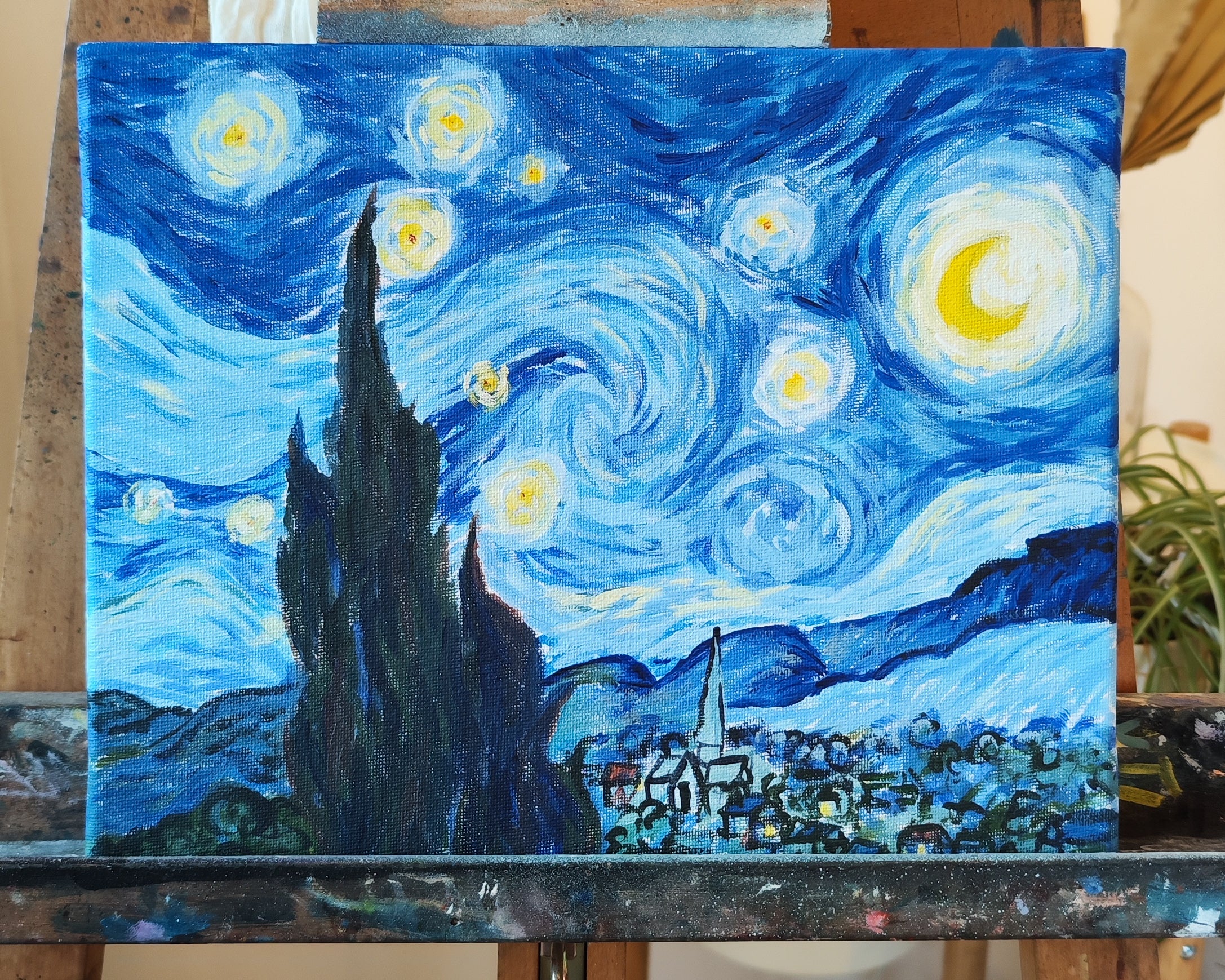 Hier ist das Beispiel für einen Kindergeburtstag zum Thema Van Gogh zu sehen. Es ist ein blaues Bild mit kleinen Häusern und einem großen Busch. Am Himmel leuchten die Sterne und der Mond.